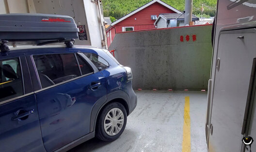 Blauer Suzuki mit Dachbox auf einem schmalen Stellplatz zwischen einem Wohnmobil und der Bordwand der Fähre nach Andenes.