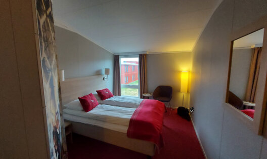 Doppelzimmer im Hotel Scandic Nordkapp mit zwei Betten, roten Kissen und Fenster.