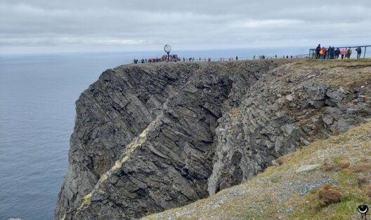 Steile Felsküste am Nordkapp mit dem Globus und zahlreichen Besuchern oberhalb des Nordmeeres.