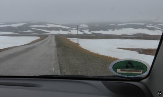 Straße über die Hochebene von Magerøya mit großen Schneefeldern und tief hängenden Wolken Mitte Juni.