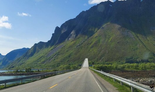 Straße und Brücke vor steilen Bergen auf der Fahrt durch die Lofoten nach Moskenes