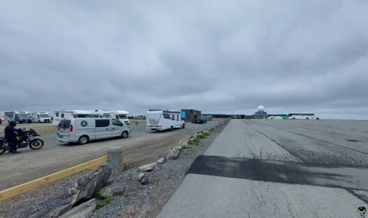 Großer Parkplatz am Nordkap mit Wohnmobilen, Reisebussen und Motorrädern unter grauem Himmel.